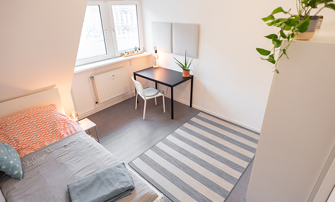 a clean student accommodation with a single bed, wardrobe, plant and small desk with a chair
