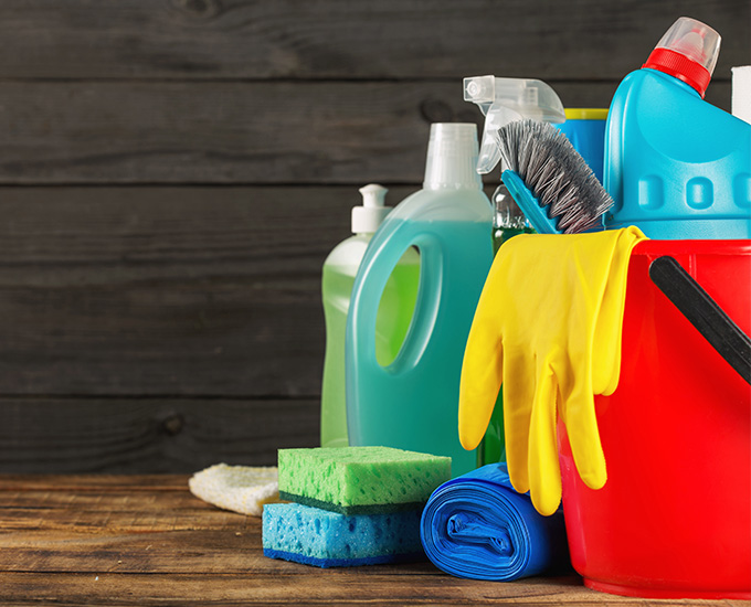 a variety of cleaning products, tools, gloves and a bucket on a wooden surface