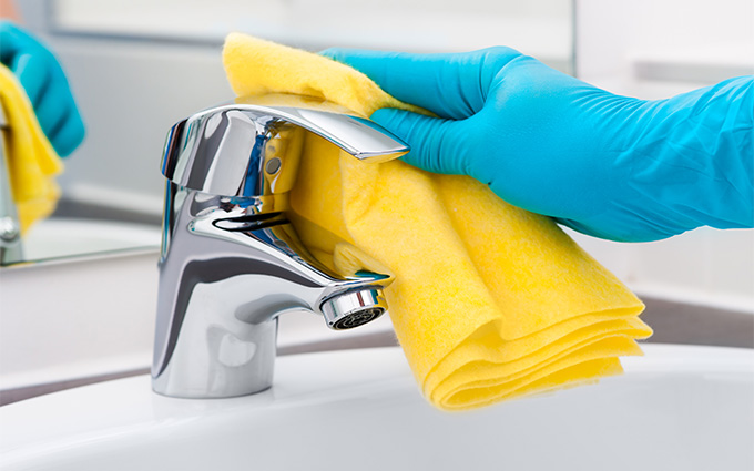 a cleaner wearing blue gloves polishing a tap with a yellow cloth